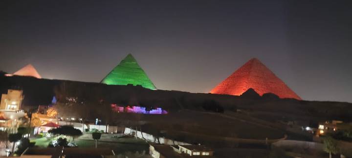 Night view of the Pyramids of Giza lit in green and red during a light show