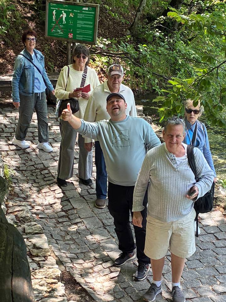 Tour group walking along cobbled path through shaded woodland, one man giving a thumbs up.