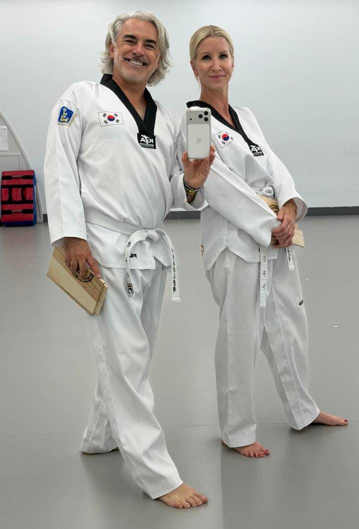 Two adults in white martial arts uniforms holding broken boards inside a dojang