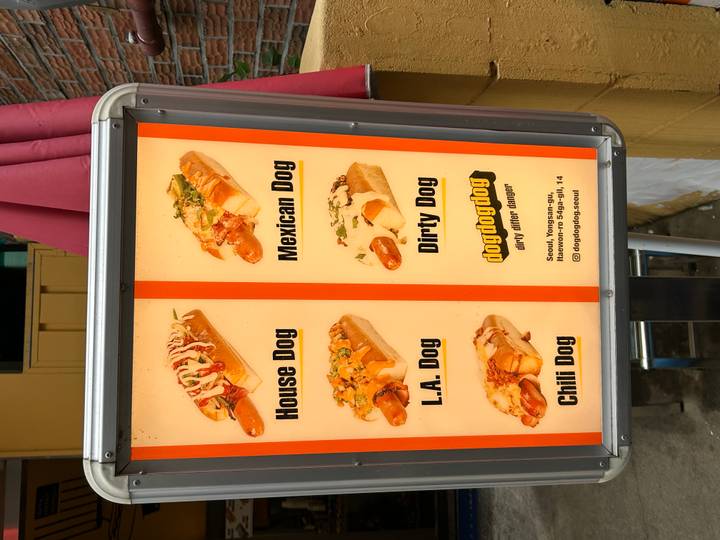 Menu signboard displaying various gourmet hot dogs on a city street