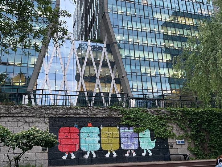 Glass office tower framed by ivy-covered wall with colorful street art robots