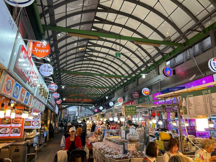 Bustling covered food market with neon signs, vendor stalls and diners in Seoul