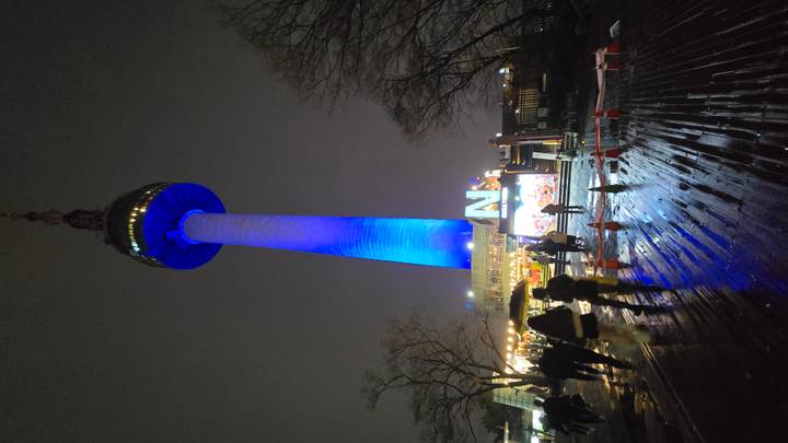 N Seoul Tower illuminated in blue rises above night visitors on a rainy plaza.