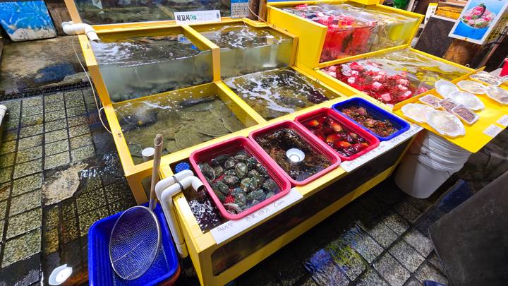 Colorful live seafood tanks and shellfish stalls at a bustling Korean fish market.