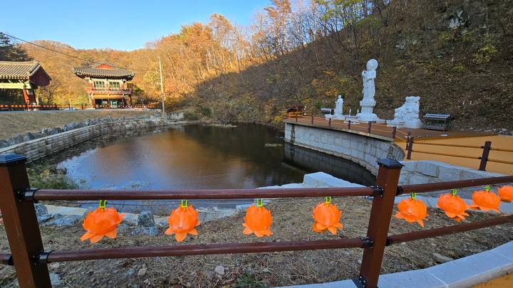 Quiet mountain temple pond decorated with bright orange lotus lanterns and stone statues in autumn forest.