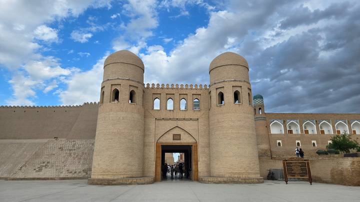 Twin brick towers mark the main gate of Khiva’s ancient city walls beneath a blue sky with clouds.