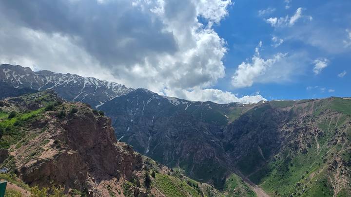 Green valleys and craggy snow-streaked peaks of the Chimgan Mountains under scattered clouds.