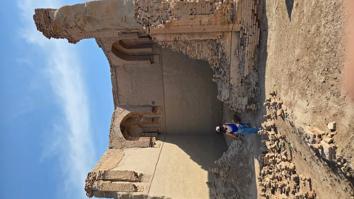 Visitor explores crumbling adobe ruins of an ancient desert fortress under clear skies.