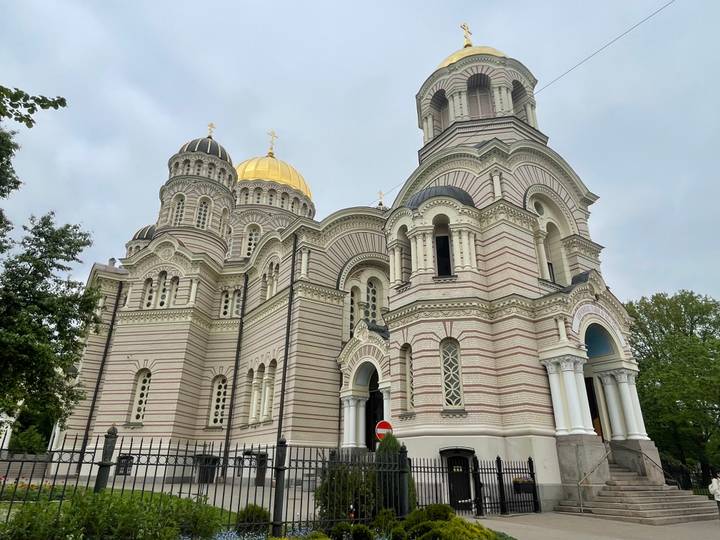 Ornate Orthodox cathedral with striped brickwork and golden dome against grey sky.