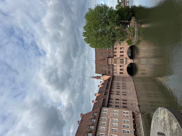 Historic hospital building spanning a quiet river under partly cloudy sky.