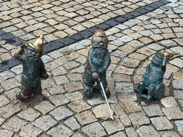 Three bronze dwarf statues on cobblestone pavement.