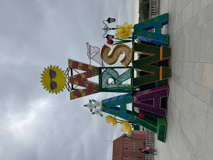 Colourful floral Warsaw sign sculpture on cloudy day in city square.