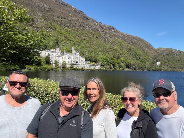 Group posing with Kylemore Abbey across the lake on a bright sunny day.