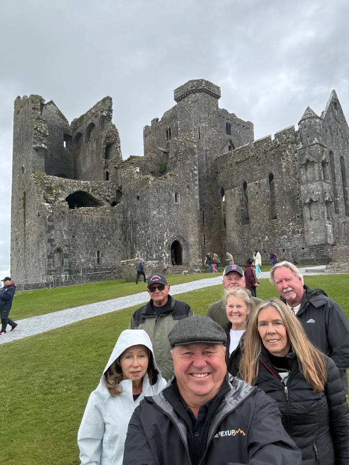 Small tour group posing happily in front of the medieval ruins of the Rock of Cashel.