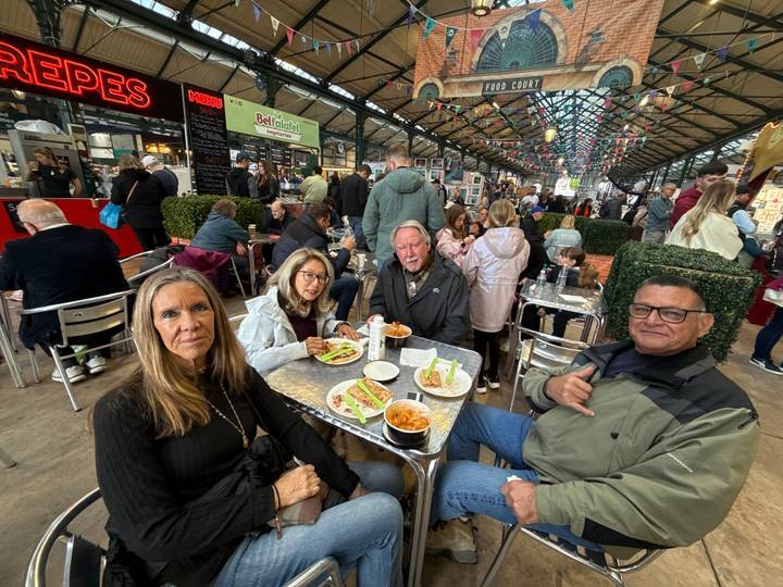 Friends enjoying lunch at a bustling indoor market food court with rows of stalls and diners.