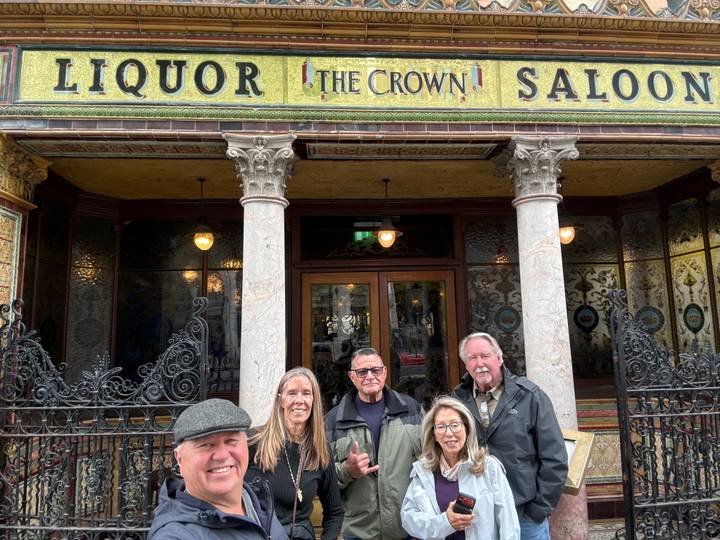 Travel group posing outside the historic Crown Liquor Saloon façade with ornate tiles.