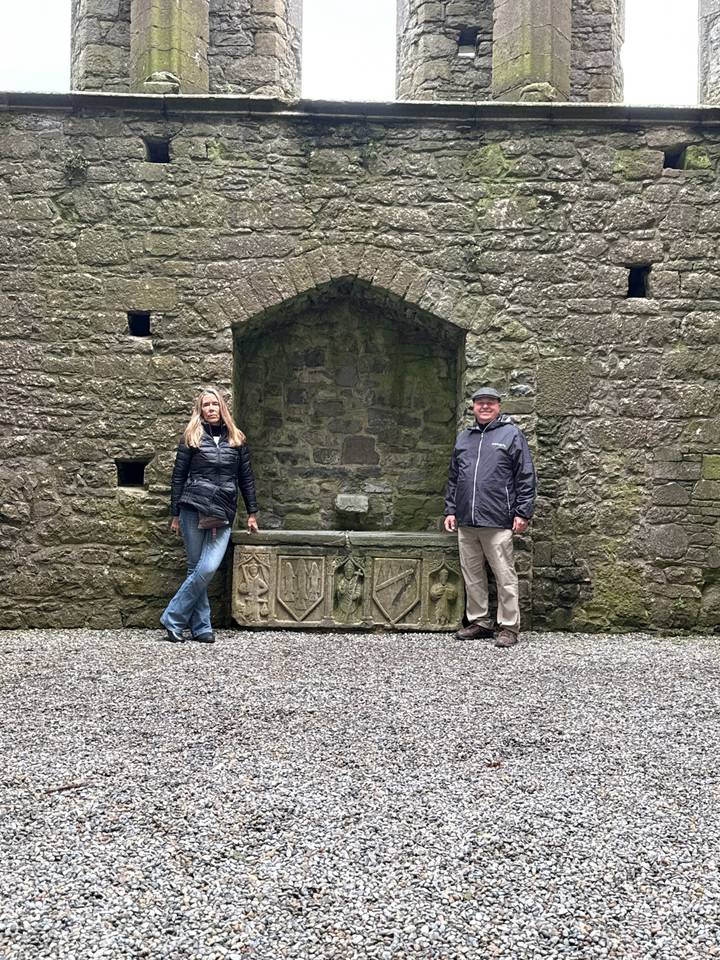 Couple posing on either side of a medieval stone fountain within a ruin courtyard.