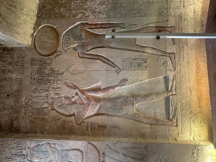 Colorful painted reliefs of ancient Egyptian deities inside a dimly lit temple corridor.