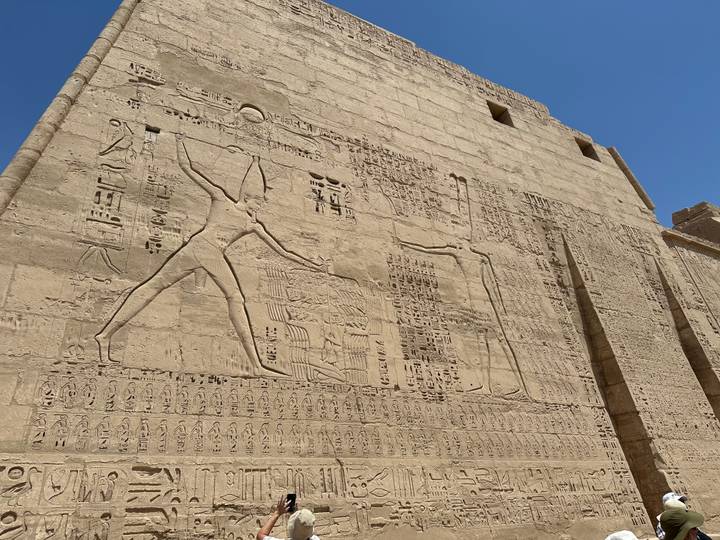 Exterior wall of an Egyptian temple carved with large-scale battle reliefs under bright sun.