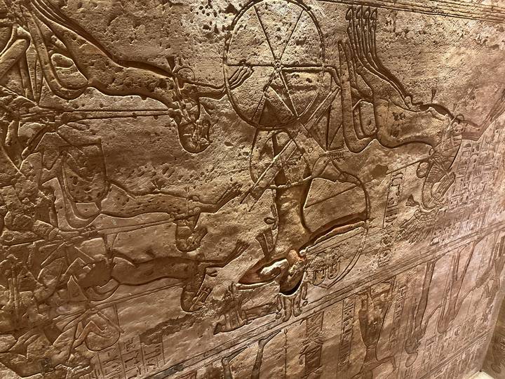 Close-up of a detailed ancient Egyptian wall relief showing a chariot scene carved in sandstone.