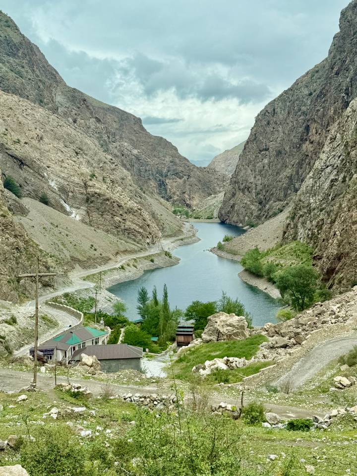 A winding canyon with steep rock walls encloses a blue river-lake, with a narrow road tracing the shoreline.