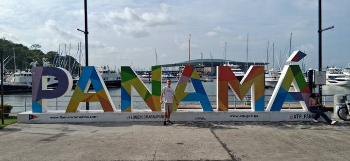 Visitor posing in front of the colorful PANAMÁ sign at a marina with boats and masts behind.