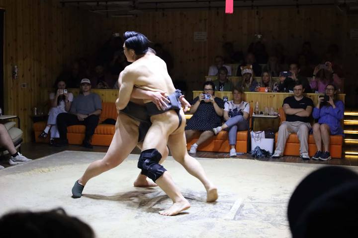 Indoor sumo demonstration with two wrestlers grappling while spectators record on phones