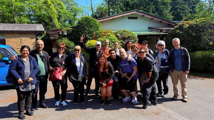 Smiling tour group posing together outside a traditional house on a sunny day