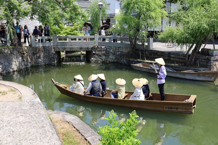Traditional flat-bottomed boat with straw-hat passengers gliding along a green canal