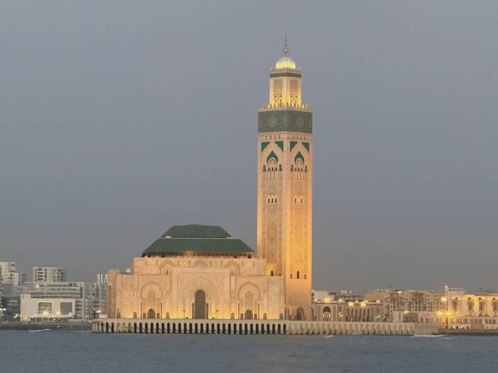 Hassan II Mosque illuminated in warm light against a dusky gray sky overlooking Casablanca