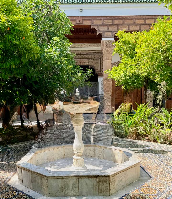 Marble fountain with silky water blur in a lush riad courtyard with zellij tiles and carved arches