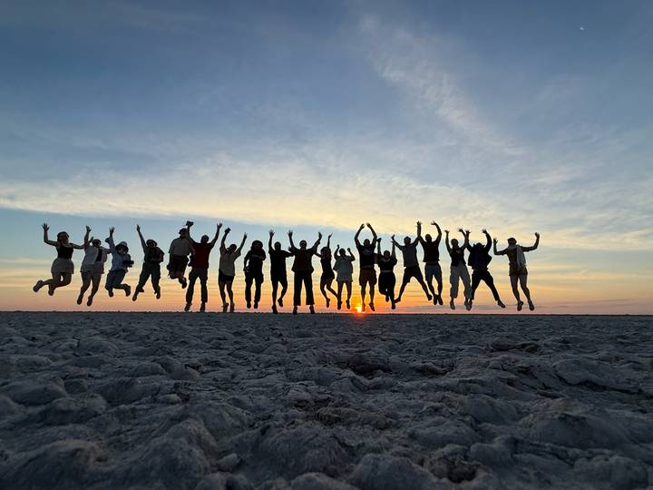 Silhouetted group jumping joyfully against sunset on vast salt pan
