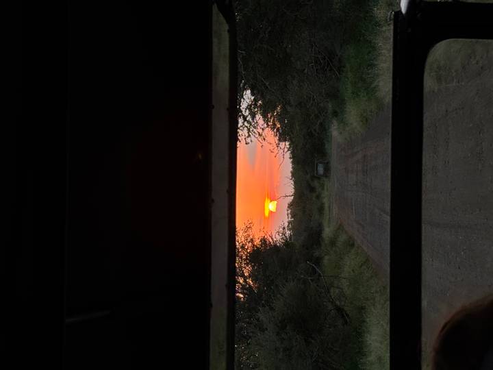 Orange sun setting beyond dirt track framed by safari vehicle window