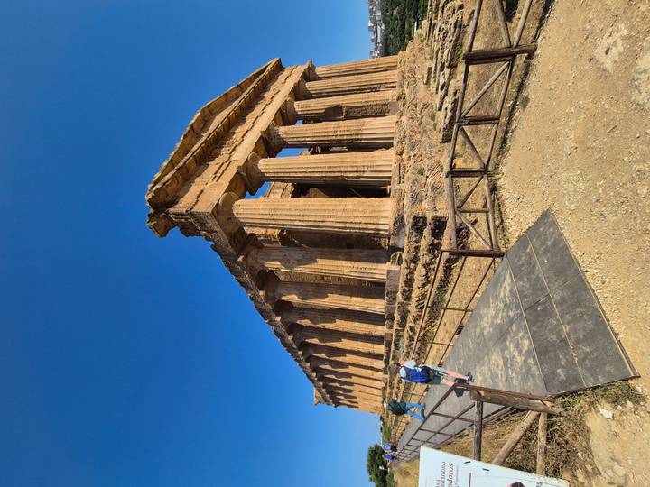 Visitors walk beside the well-preserved Doric Temple of Concordia in Agrigento’s Valley of the Temples under a clear blue sky.