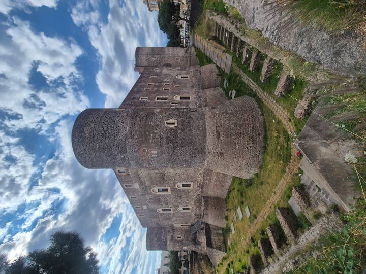 Massive stone towers and walls of Castello Ursino in Catania under a partly cloudy sky.