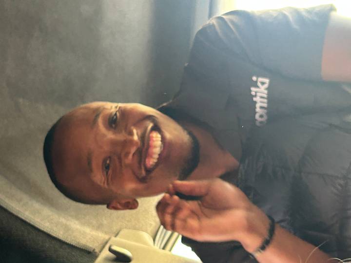 Slightly blurry close-up of a smiling safari guide wearing a branded shirt inside a vehicle.