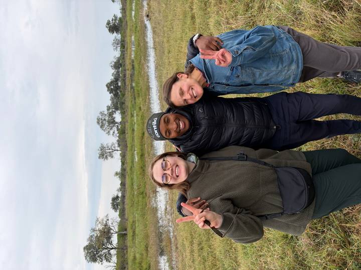 Friends embrace and flash peace signs beside a wetland with cloudy skies