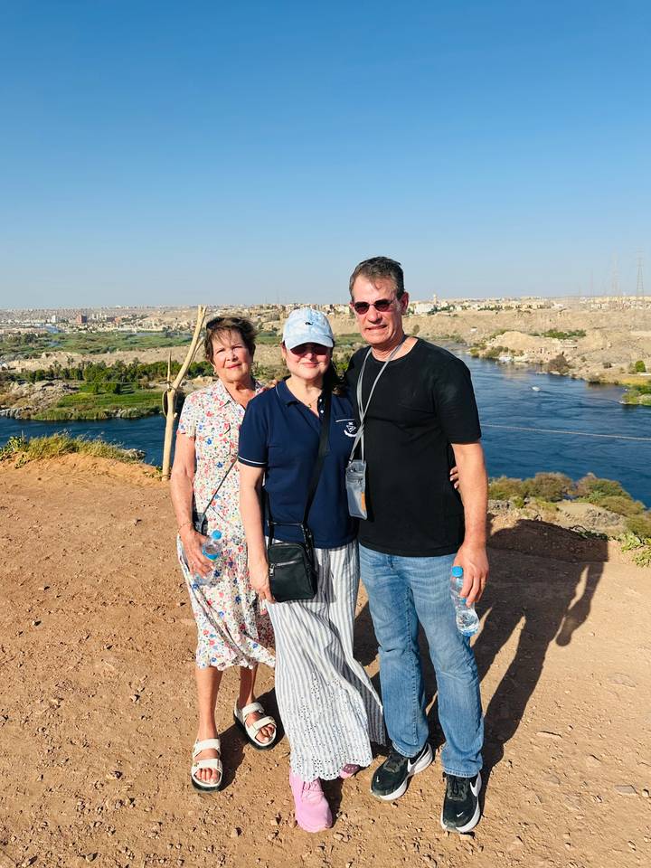 Three travelers pose on a desert bluff overlooking the broad Nile River near Aswan.