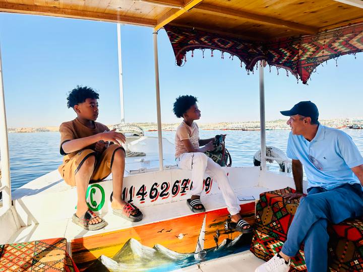 A felucca captain chats with two children seated on a white sailboat on the Nile.