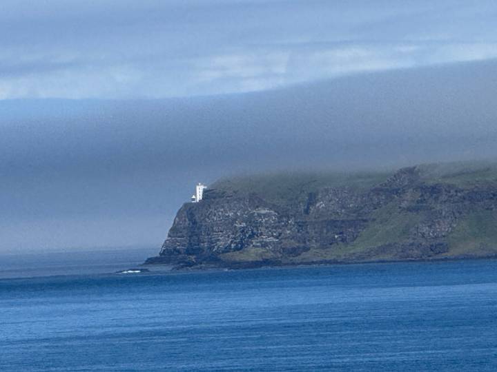 Distant lighthouse on a mist-covered cliff above calm blue ocean
