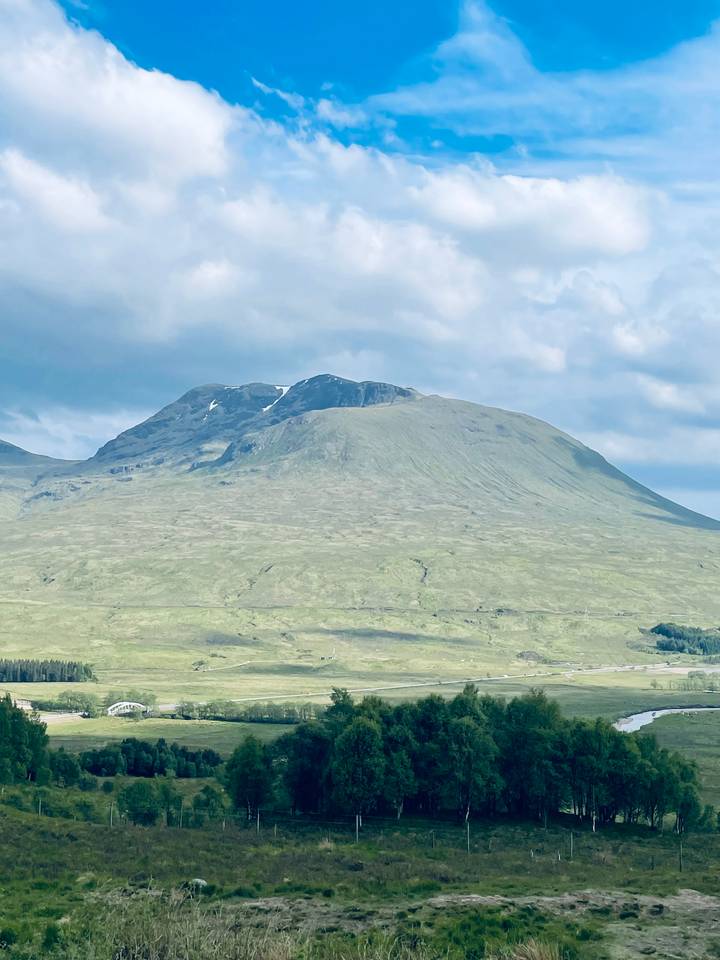 Gentle green mountain slopes under a cloudy blue sky in the Scottish Highlands.