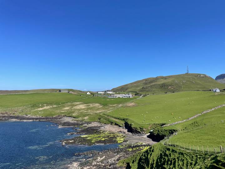 Rural coastal hamlet with rolling green pastures and blue sea under a clear sky.