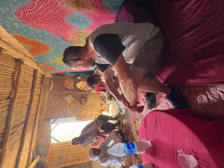 Travellers sit cross-legged on colorful rugs inside a traditional Berber clay house sharing conversation.