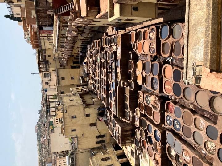 View over rows of circular tanning pits in a traditional Moroccan leather tannery surrounded by yellowed buildings.