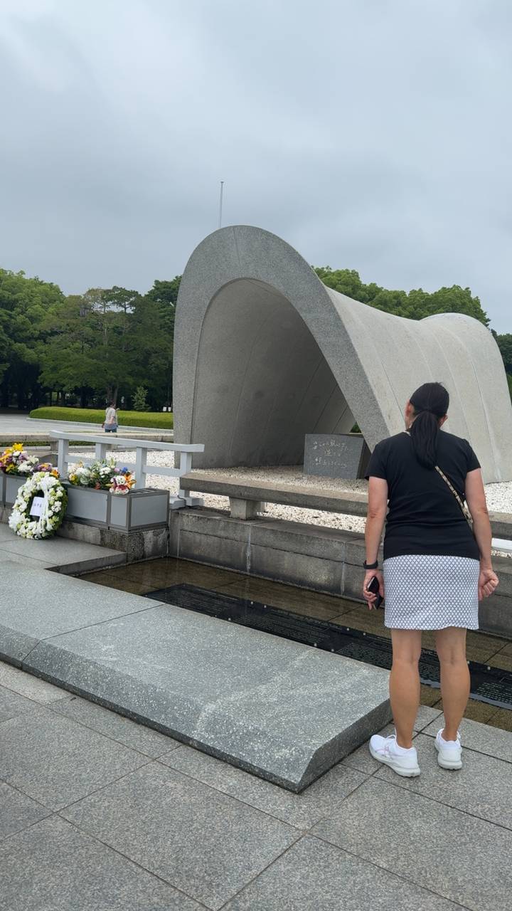Visitor looking at the Cenotaph in Hiroshima Peace Park with floral wreaths nearby.