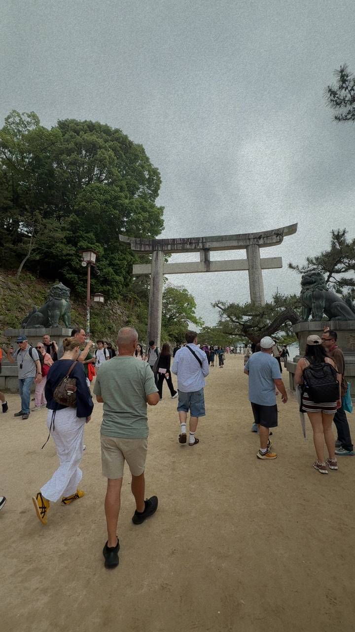 Crowd passing under a large stone torii gate flanked by lion statues at a Japanese shrine entrance.