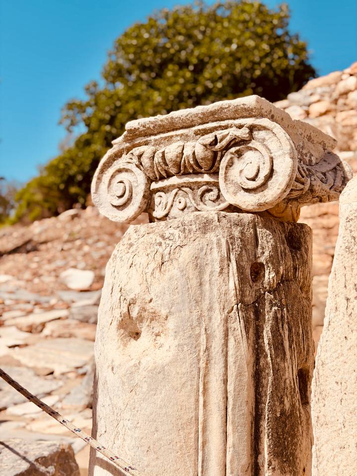 Close-up detail of an ornate Ionic capital carved in weathered stone at an archaeological site.
