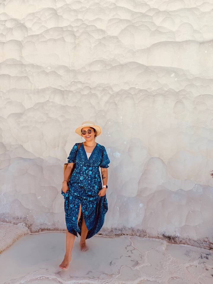 Woman in a blue dress and sunhat smiles against the creamy mineral formations of Pamukkale.