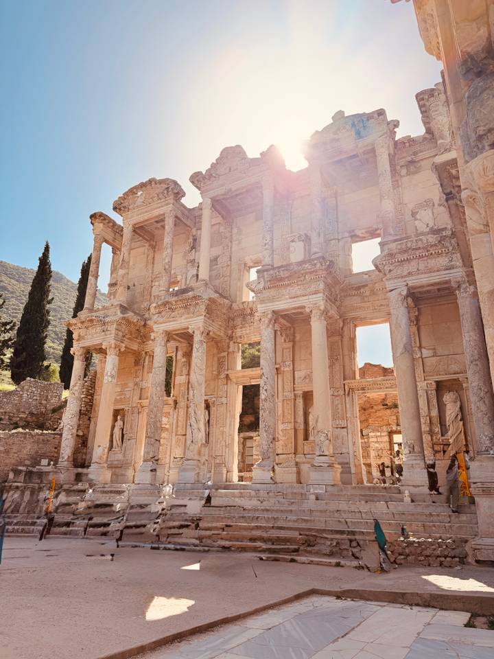 Sunlit façade of the ancient Library of Celsus with dramatic columns and statues.