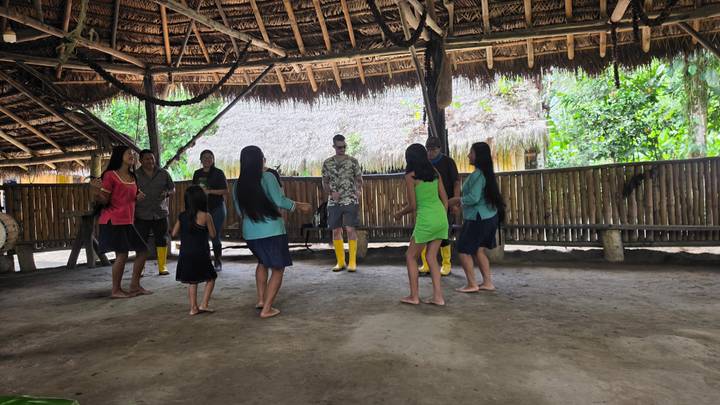Visitors join local community members in a barefoot traditional dance inside a thatched community hall.